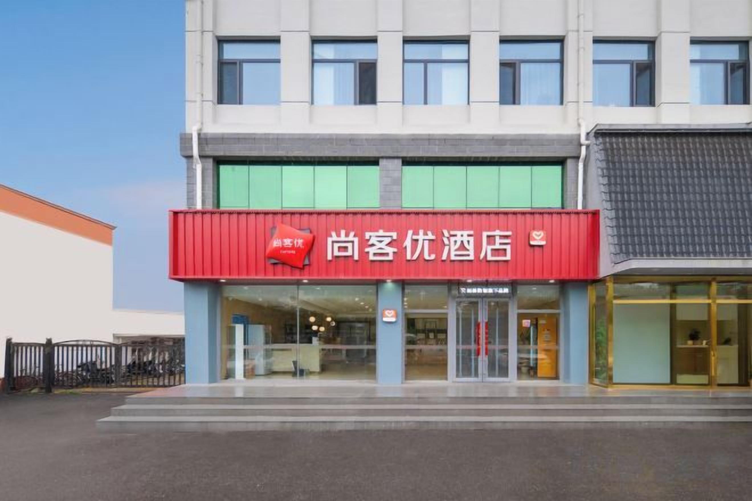 A hotel with a red signboard, a glass entrance, and a modern facade.