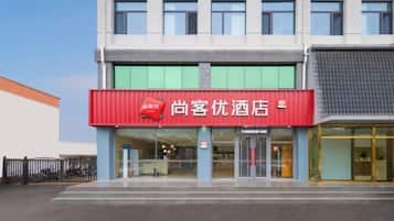 A hotel with a red signboard, a glass entrance, and a modern facade.