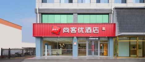 A hotel with a red signboard, a glass entrance, and a modern facade.