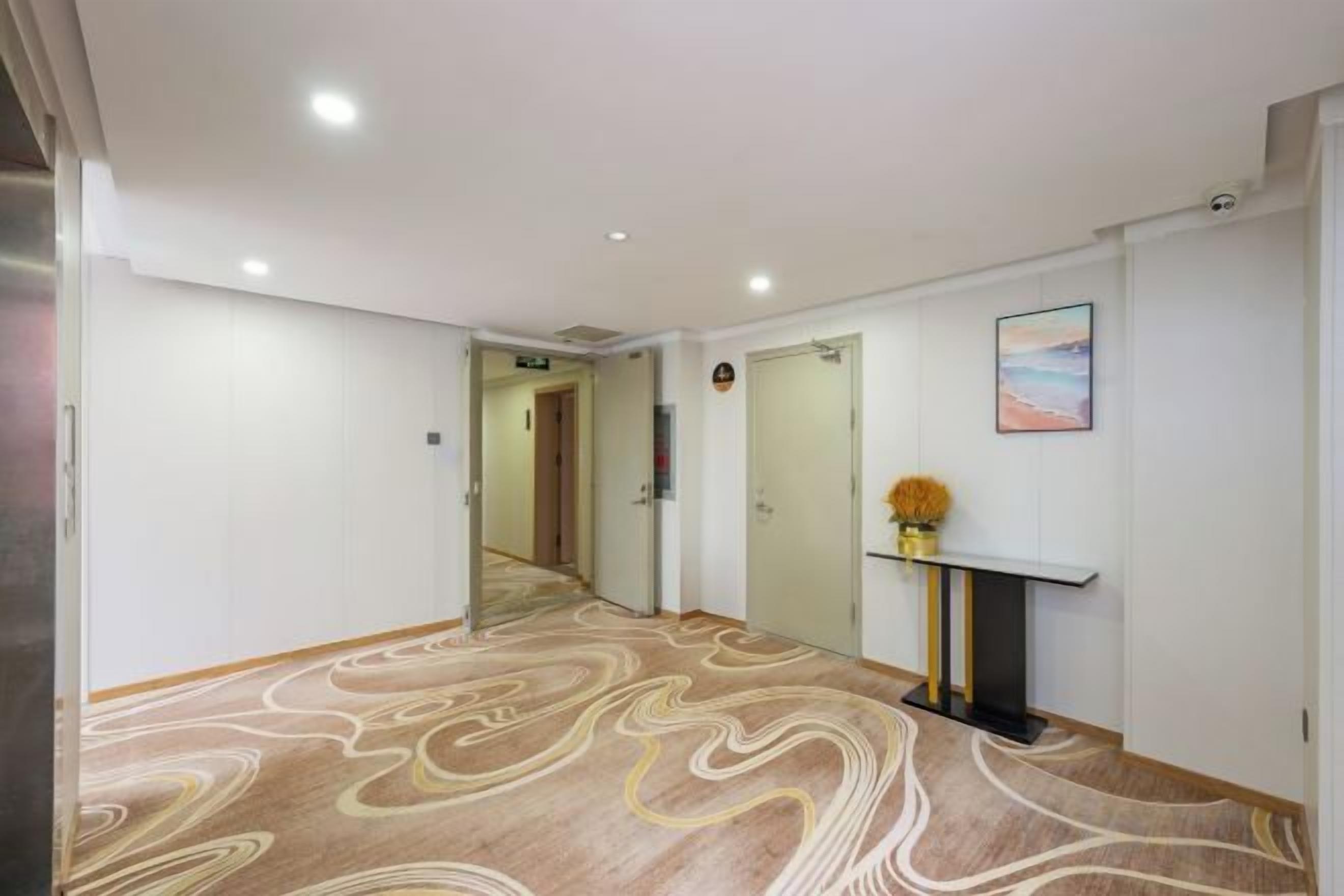 A hotel hallway with a patterned carpet, a fireplace with a vase of flowers, and a painting on the wall.