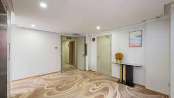 A hotel hallway with a patterned carpet, a fireplace with a vase of flowers, and a painting on the wall.