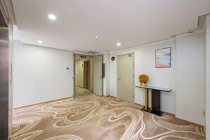 A hotel hallway with a patterned carpet, a fireplace with a vase of flowers, and a painting on the wall. - Shankee Express Hotel (Beijing Miyun Guoyuan) (Beijing)
