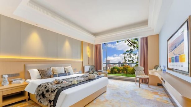 A hotel room with a large bed, a desk, a chair, a window with a view of greenery, and a wall-mounted TV. - Guangbin Mantiao Hotel (Foshan Lishui Wanli Plaza) (Foshan)