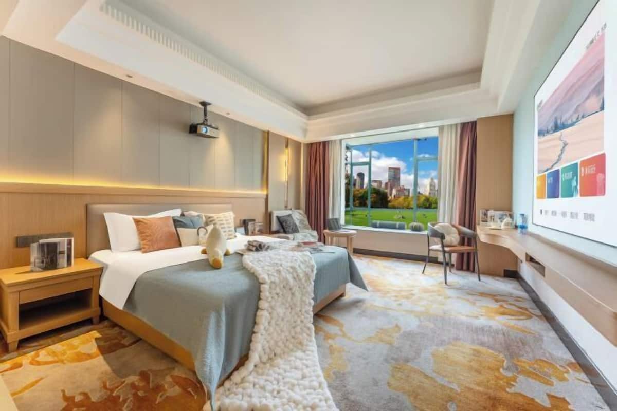 Habitación de hotel con una cama grande, un escritorio, una silla y vistas a un paisaje urbano.