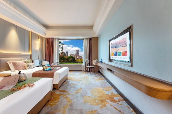 Habitación de hotel con dos camas, un escritorio, una silla, un televisor y vistas a la ciudad.
