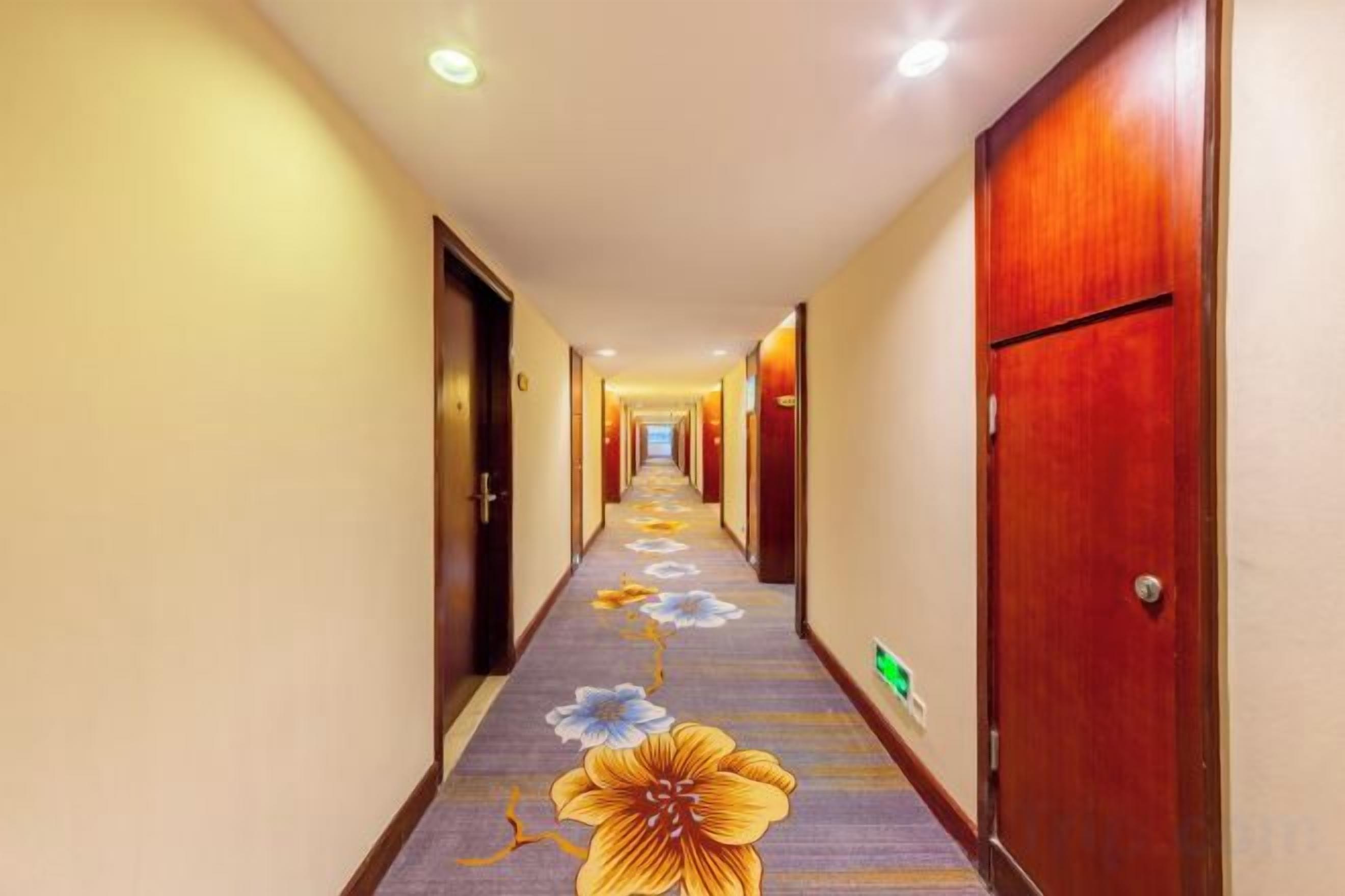Un pasillo de hotel con puertas a ambos lados, una alfombra con motivos florales y un cartel verde en la pared.
