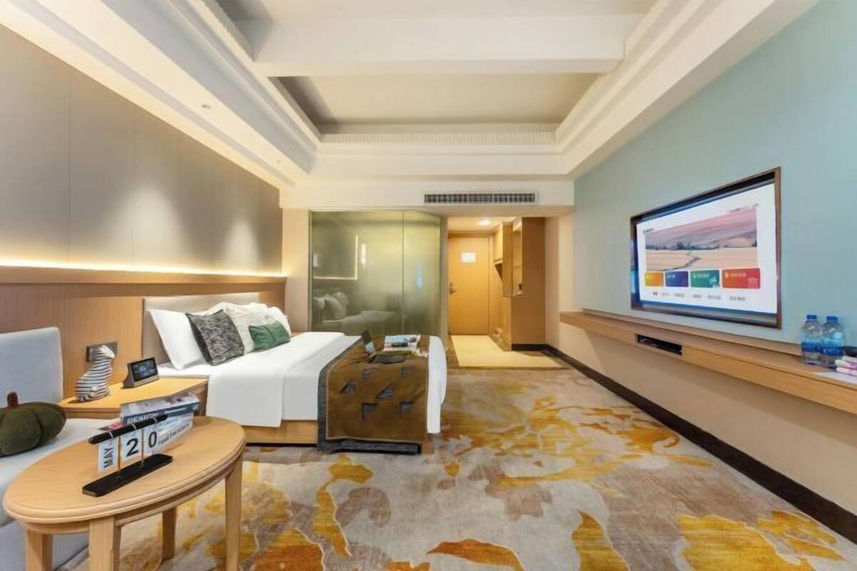 Habitación de hotel con cama, televisor, una mesita con reloj y piso alfombrado.