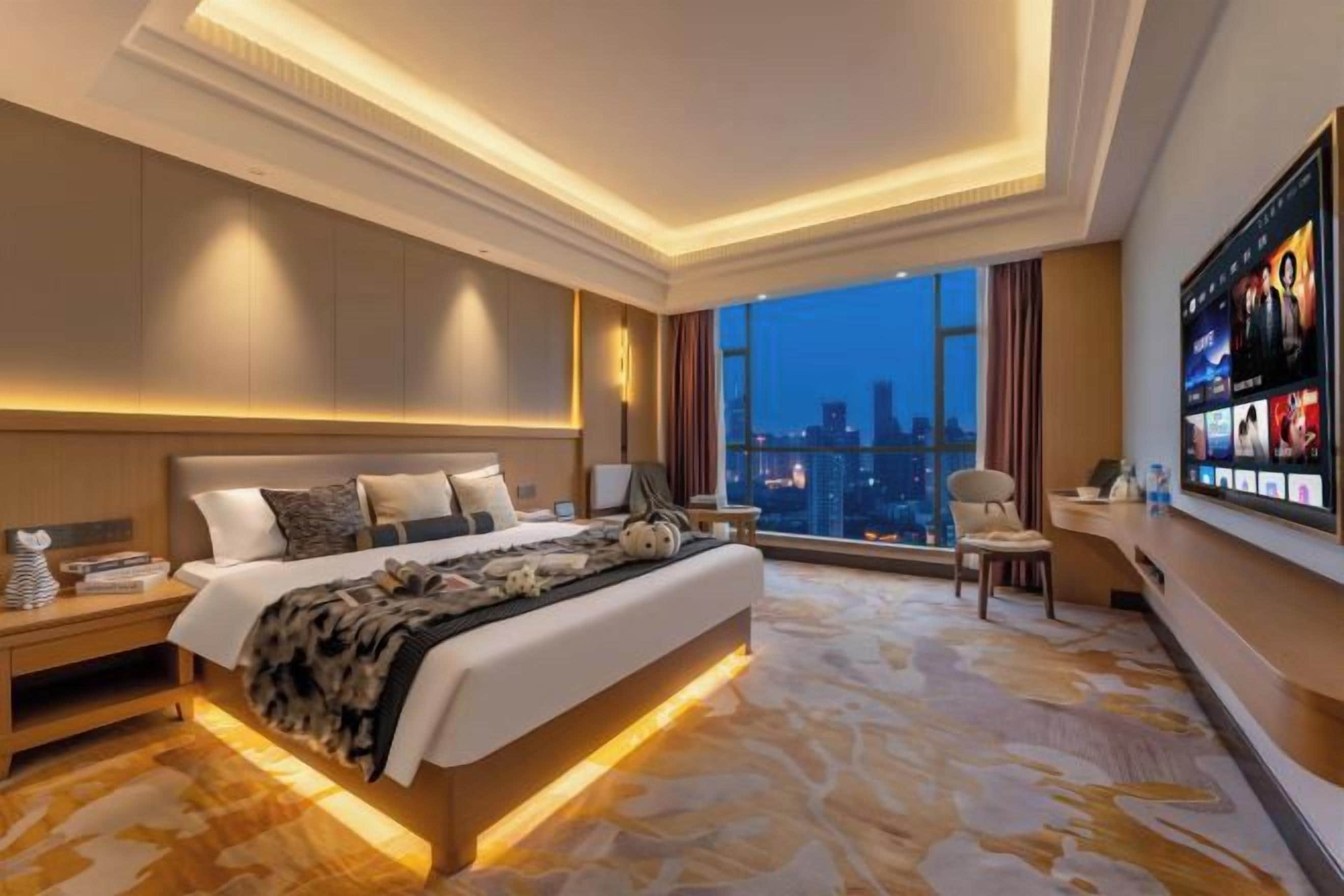 A modern hotel room with a large bed, a city view, a flat-screen TV, and a desk with a chair.