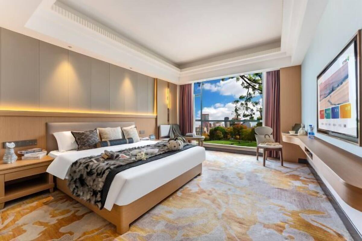 Habitación de hotel con una cama grande, un escritorio, una silla y vistas al exterior.