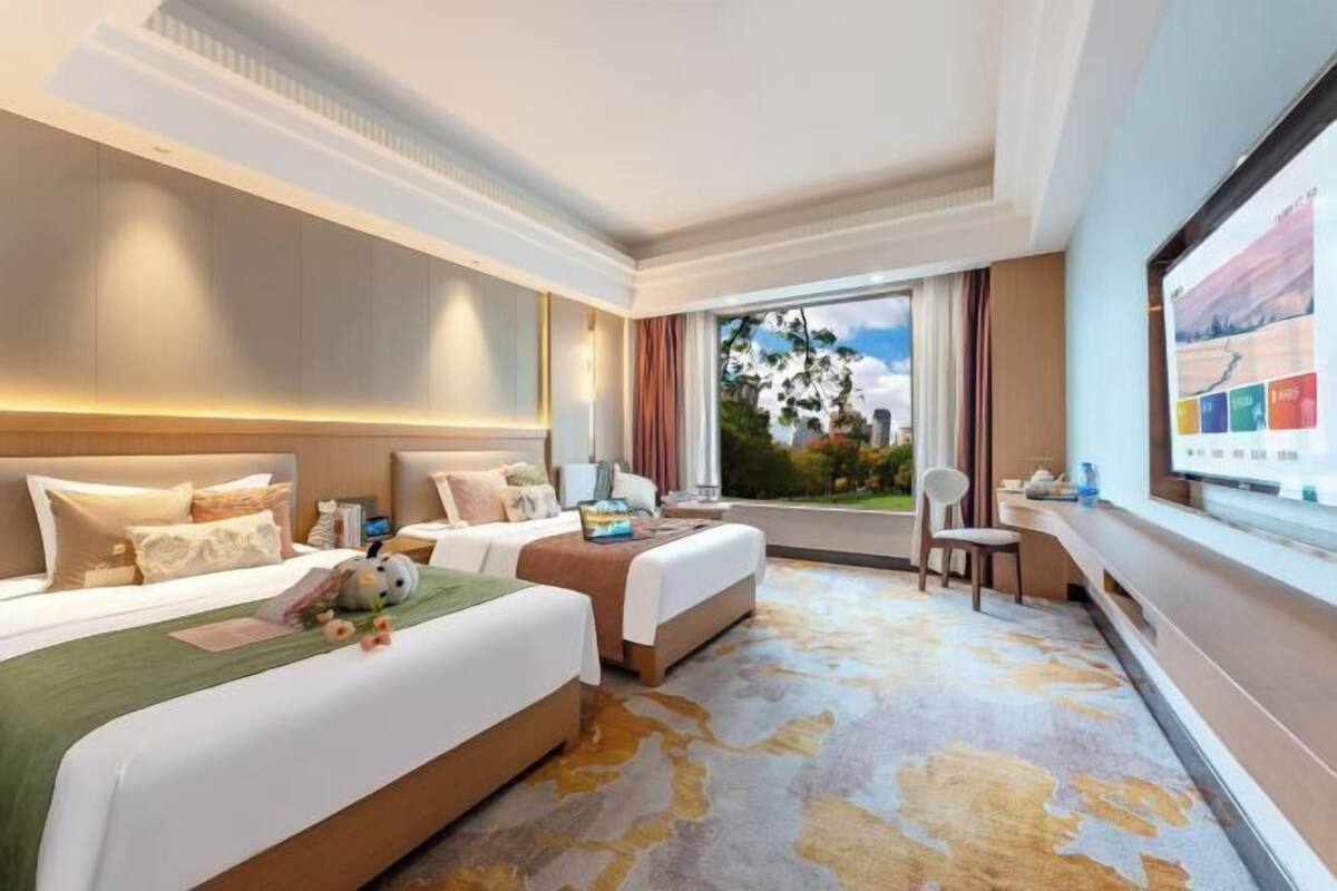 Habitación de hotel con dos camas, un escritorio, una silla, un ventanal con vistas y un televisor.