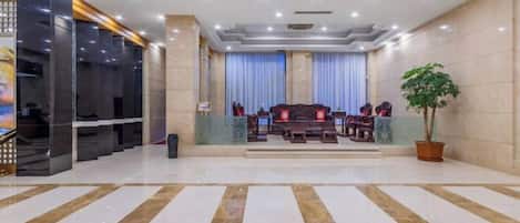 A hotel lobby with a reception desk, seating area, and a large potted plant.