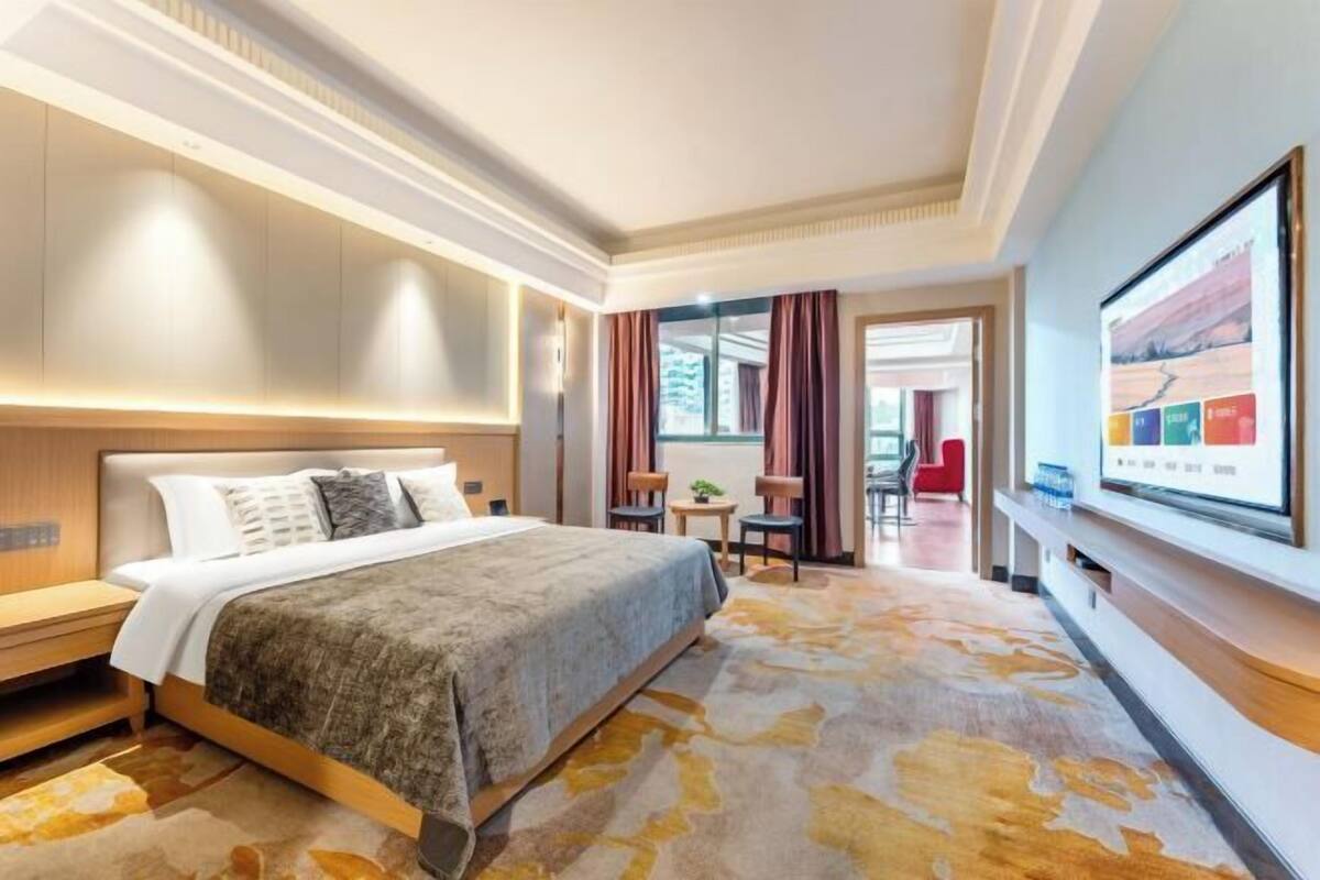 Habitación de hotel con cama, escritorio, silla, televisor y vista al exterior.