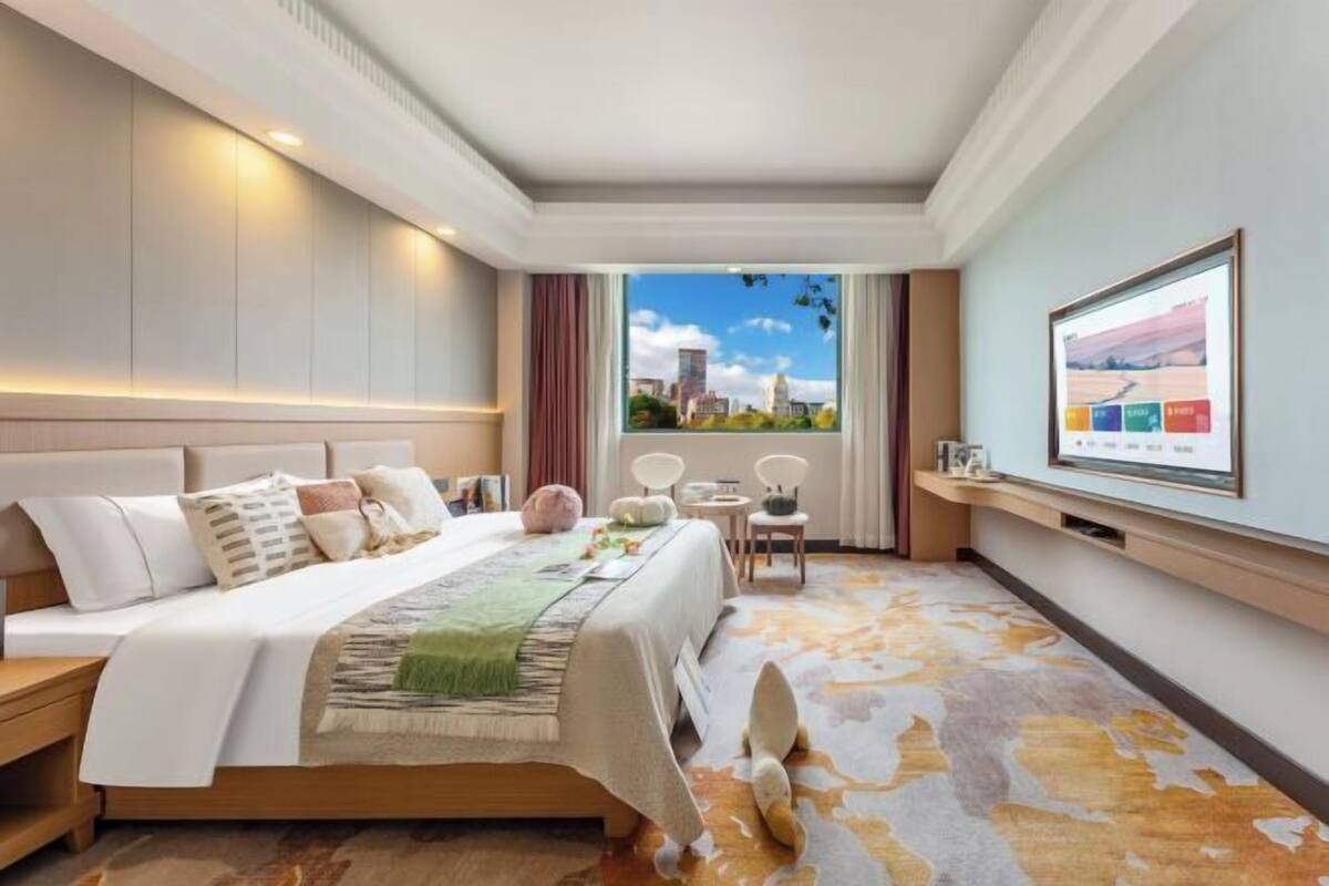 Habitación de hotel con una cama grande, vista a la ciudad, una mesita y un televisor en la pared.