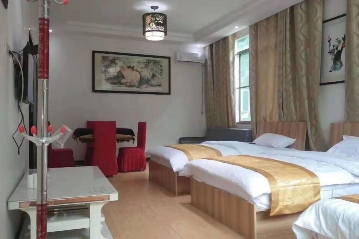 A hotel room with two beds, a desk, and a chair. There is a painting on the wall and a window with curtains.