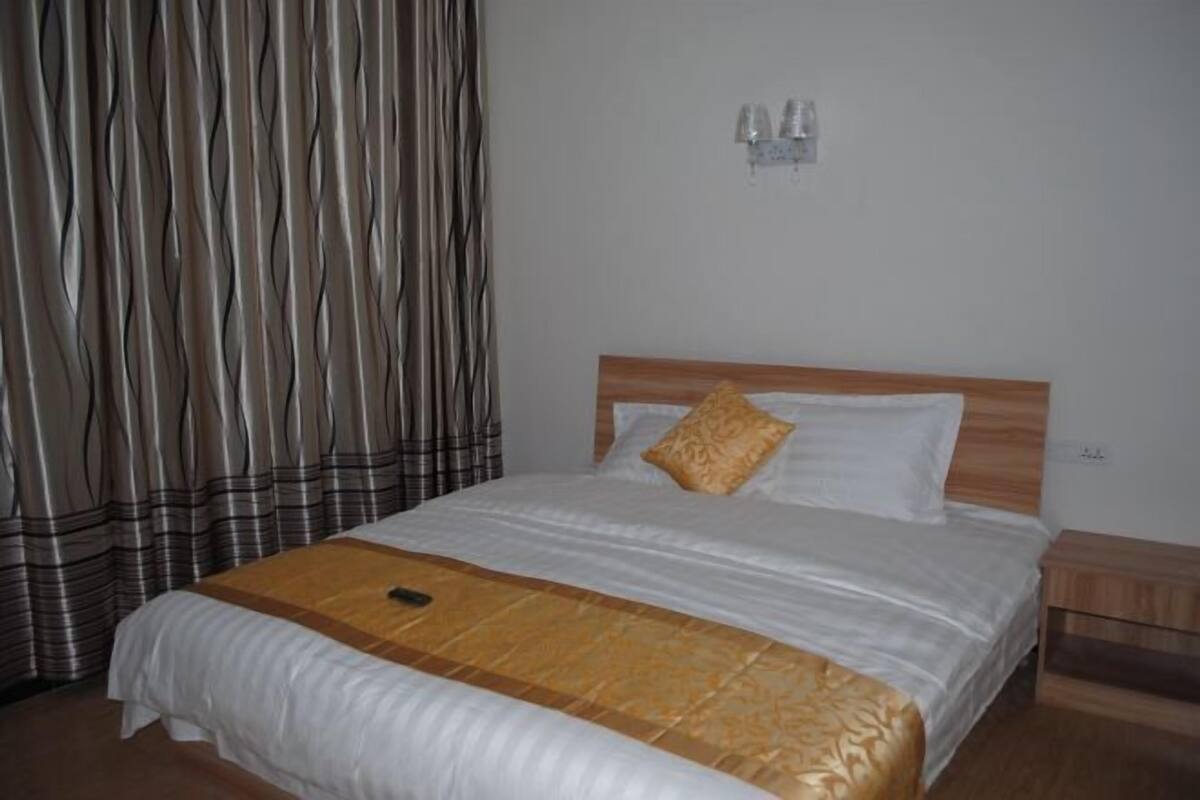 A neatly made bed with a wooden headboard, a patterned throw blanket, and a remote control on the bed.