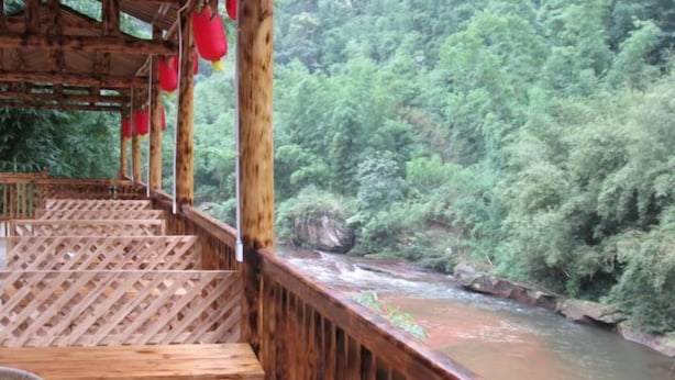 A wooden deck with a view of a river and dense greenery. - Puyuan Xiangu Hotel (Chishui)