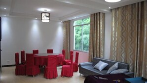 A room with a round table and red chairs, a grey sofa with cushions, and a window with curtains. - Puyuan Xiangu Hotel (Chishui)