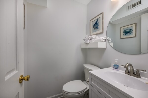 A bathroom with a white toilet, a sink with a mirror, and framed artwork on the wall.