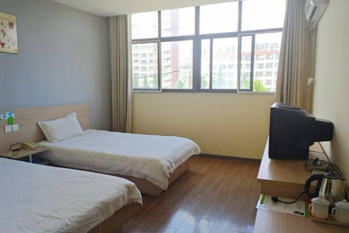 A hotel room with two beds, a desk with a computer, and a window with a city view.