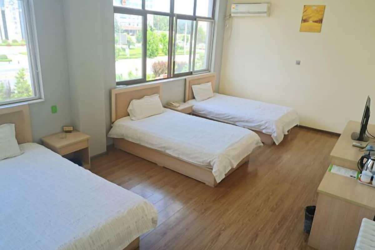 A room with two single beds, a desk, and a window with a view of greenery.