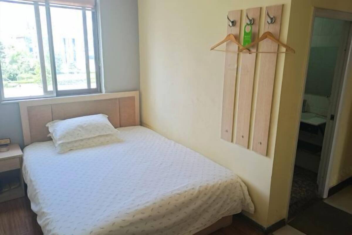 A bedroom with a bed, a nightstand, a window, and a wall-mounted coat rack.