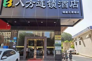 A hotel entrance with a glass door, a sign above the door, and a parking area with cars and motorcycles. - 8 Inn (Dongguan)