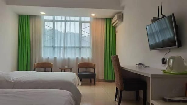 Une chambre d’hôtel avec deux lits, un bureau, une chaise, une télévision et une fenêtre avec des rideaux.