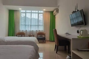 Ein Hotelzimmer mit zwei Betten, einem Schreibtisch, einem Sessel, einem Fernseher und einem Fenster mit Vorhängen.