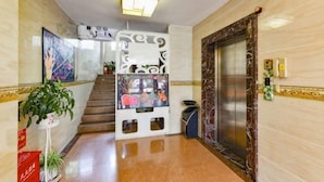 Un hall d’hôtel avec un escalier, un ascenseur, un comptoir d’accueil et une plante en pot.