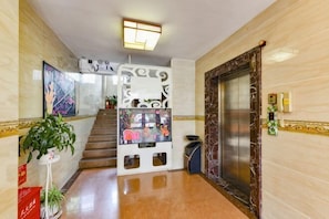 A hotel lobby with a staircase, an elevator, a reception desk, and a potted plant. - 8 Inn (Dongguan)