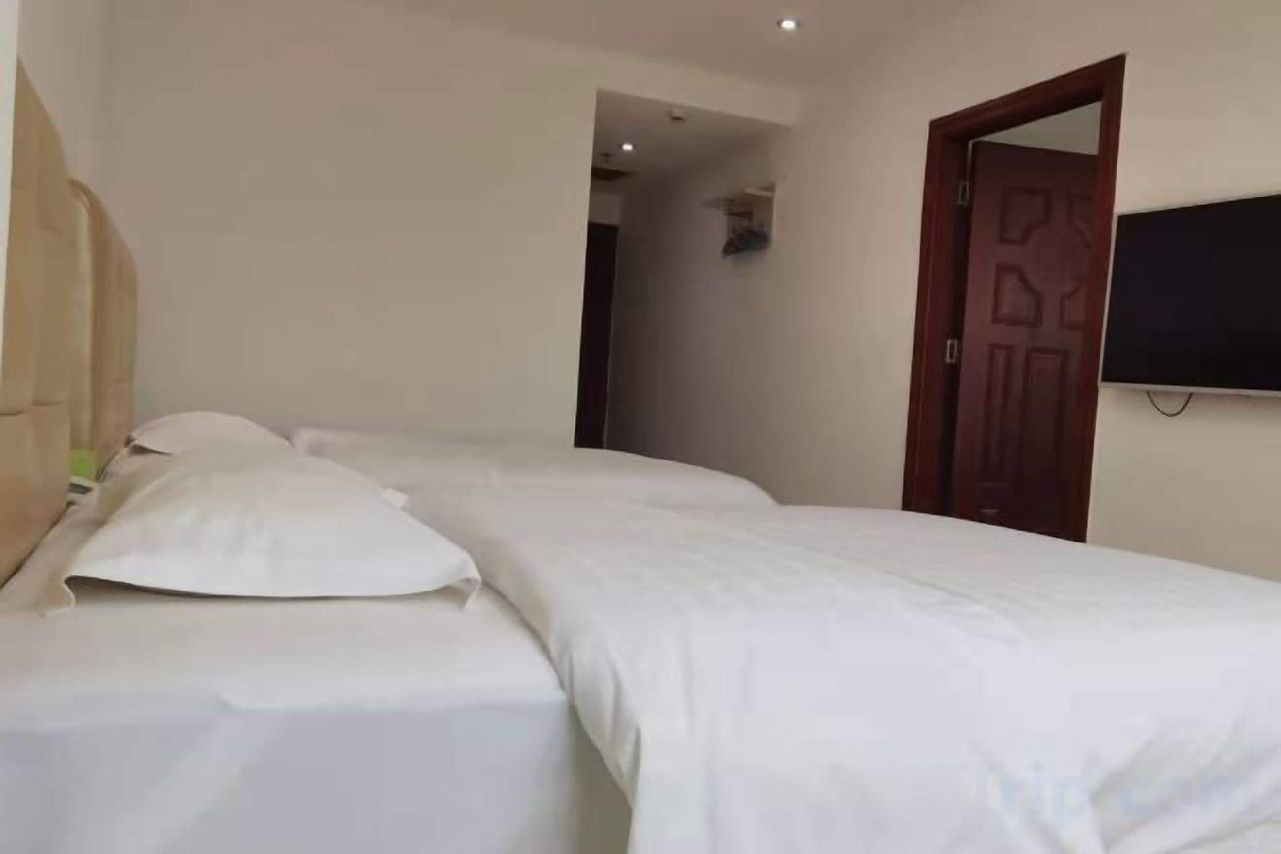 Une chambre d’hôtel avec deux lits, un téléviseur fixé au mur et une porte donnant sur une autre pièce.