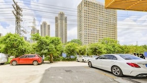 Un parking avec des voitures, des arbres et de grands immeubles en arrière-plan.