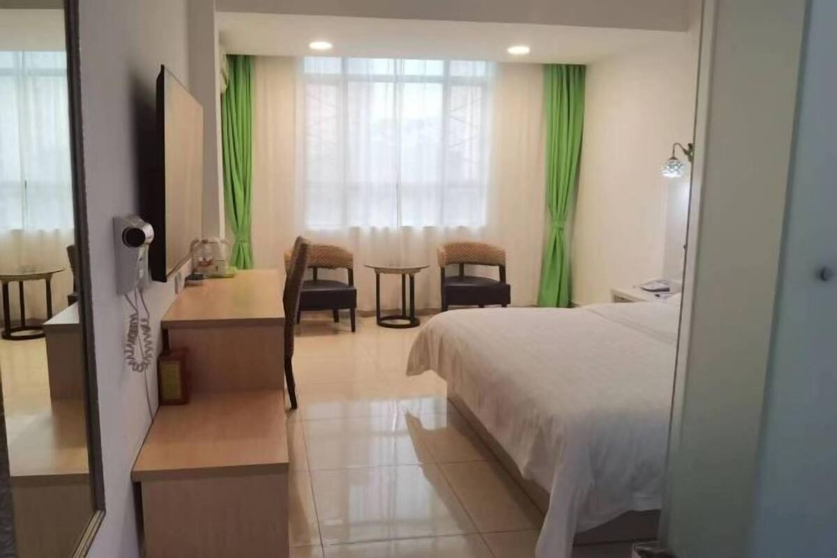 A hotel room with a bed, two chairs, a small table, a desk, a mirror, and a window with curtains.