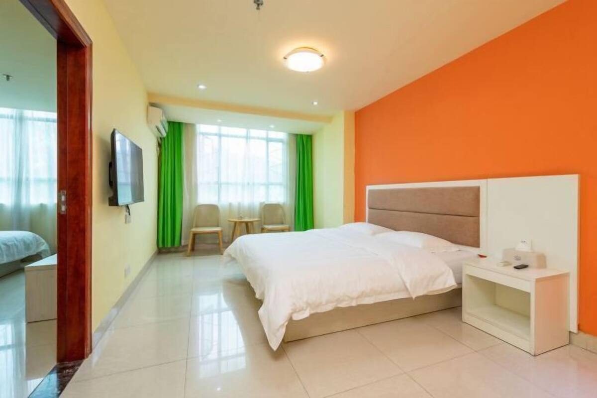 A hotel room with a bed, bedside table, TV, and a view of the outside.
