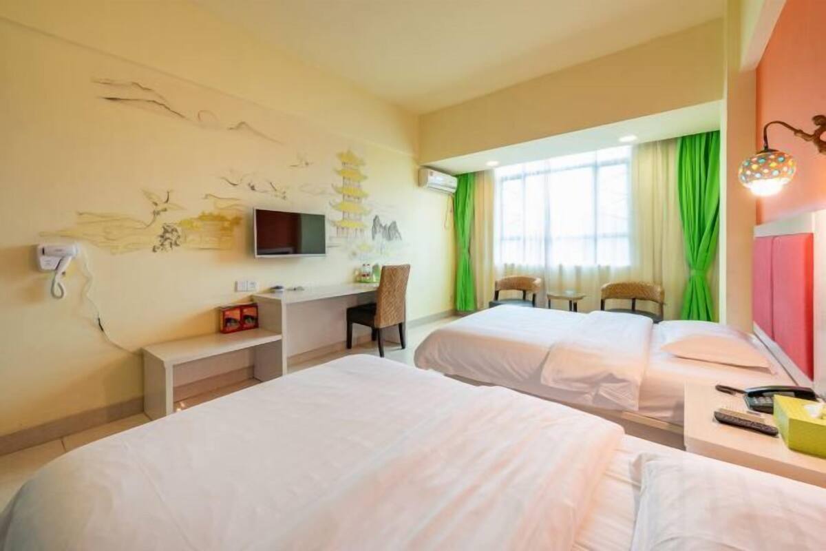 A hotel room with two beds, a desk, a chair, a TV, and a window with curtains.