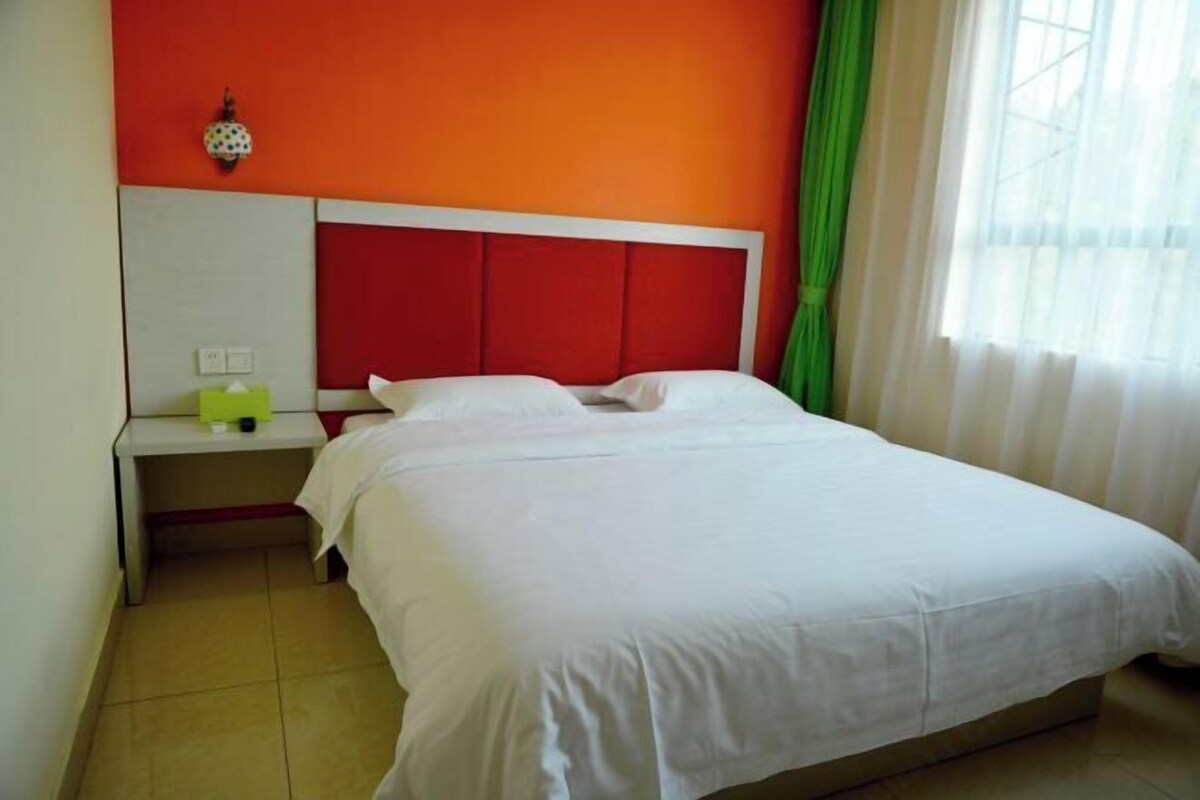 A single-bed room with a white bed, red headboard, and a small bedside table with a green lamp.