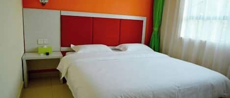 A single-bed room with a white bed, red headboard, and a small bedside table with a green lamp.