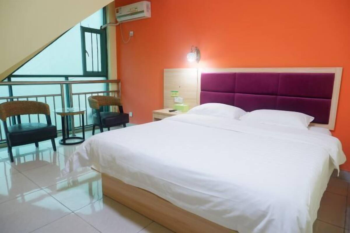 A hotel room with a bed, a nightstand, a chair, a small table, and a balcony with chairs.