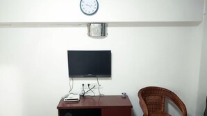 Ein Zimmer mit an der Wand befestigtem Fernseher, einem Holztisch mit Fernbedienung und einem Korbstuhl.