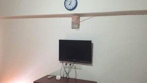Ein Zimmer mit Holzbalkendecke, einer Uhr, einem an der Wand befestigten Flachbildfernseher und einem Holztisch mit einem weißen Gegenstand darauf.