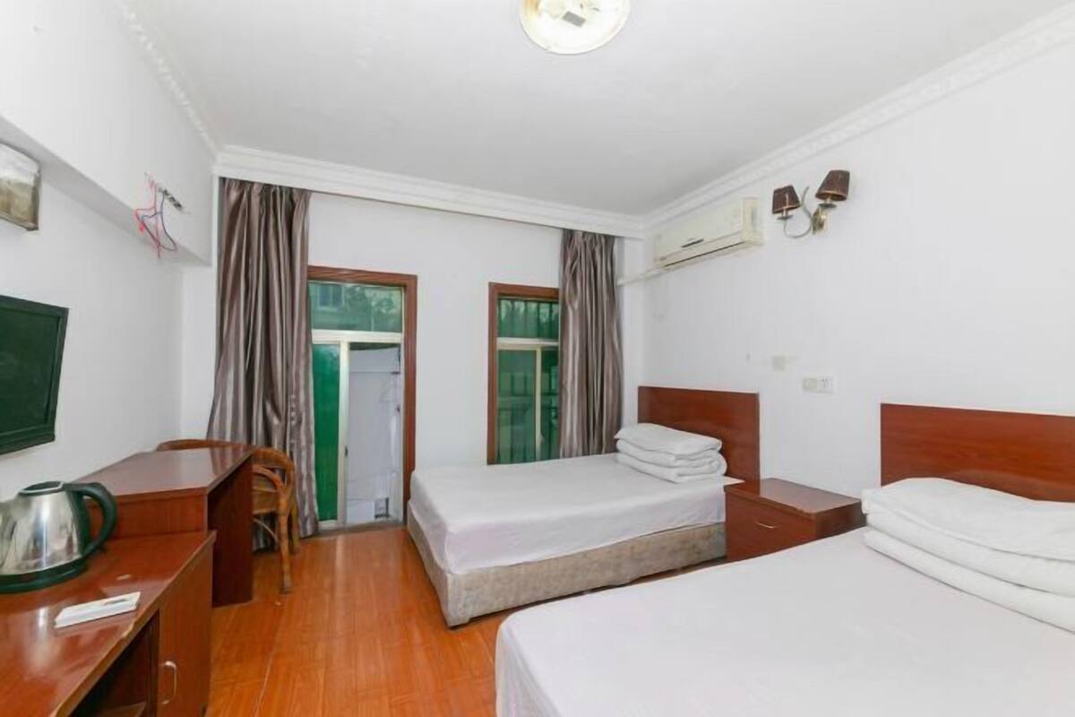 A hotel room with two single beds, a desk with a chair, a television, and a window with curtains.