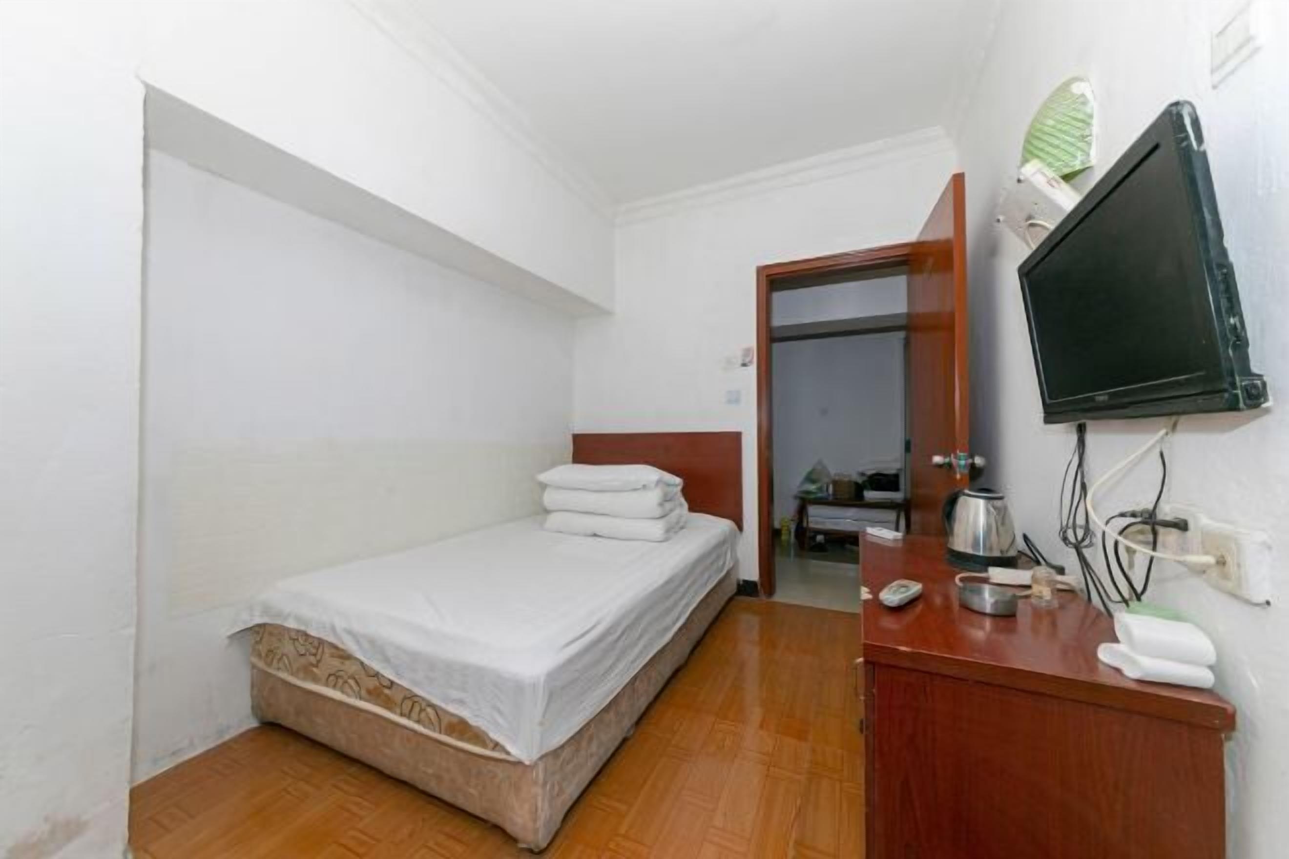A small, clean room with a single bed, a wooden dresser, a television, and a mirror.