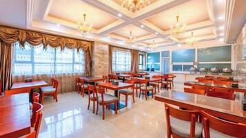 A spacious dining area with multiple tables and chairs, large windows with curtains, and a chandelier.