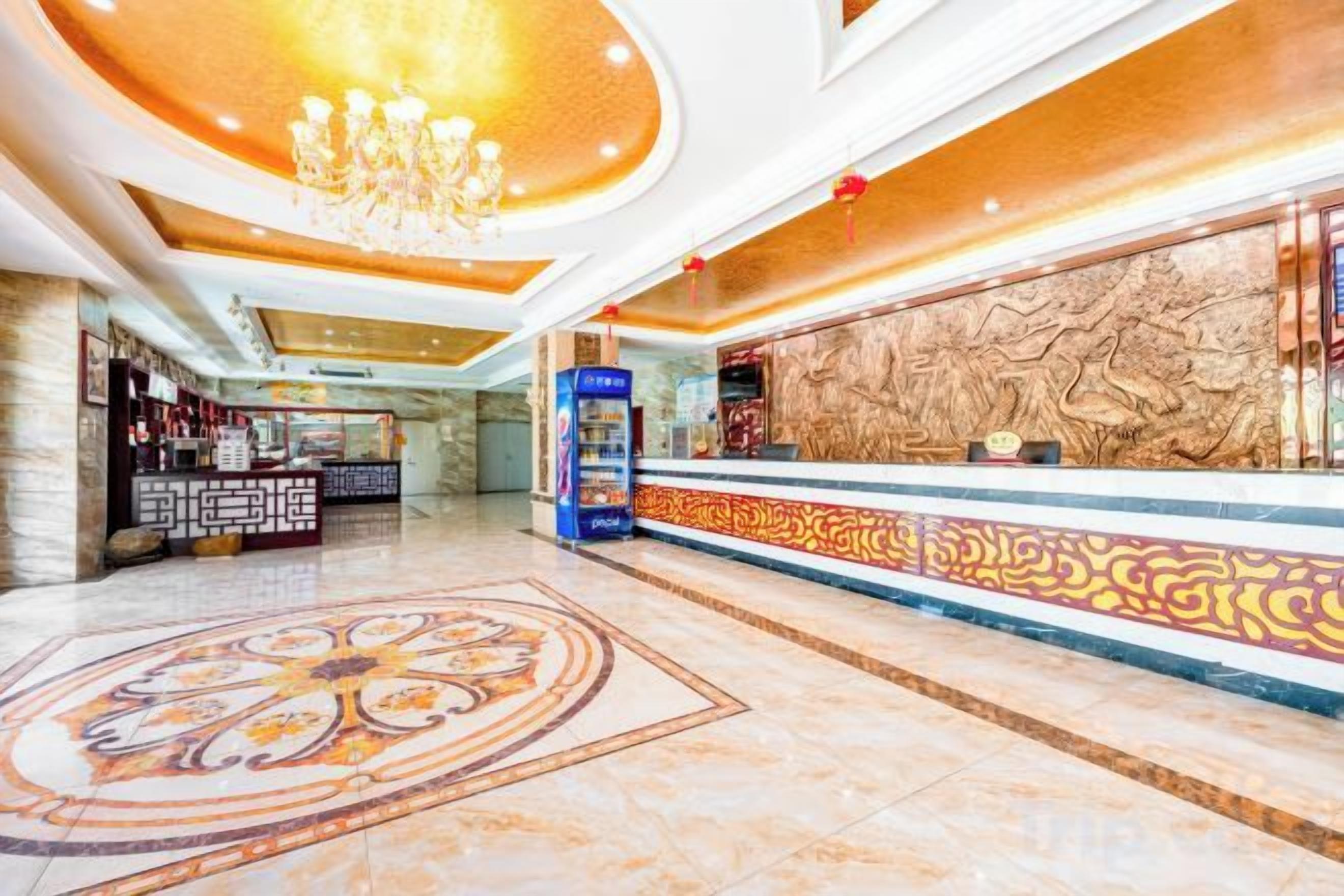 A hotel lobby with a reception desk, a chandelier, and a decorative floor pattern.
