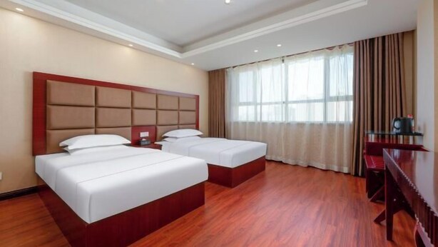 Une chambre d’hôtel avec deux lits, un plancher en bois, une grande fenêtre avec des rideaux et un bureau avec une chaise.