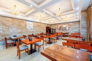 Un comedor de hotel con varias mesas y sillas, candelabros y una pared de mármol.