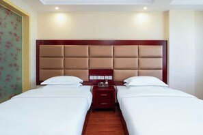 A hotel room with two beds, a wooden headboard, a nightstand, and a floral-patterned wall. - Korla Apricot Business Hotel (Korla)