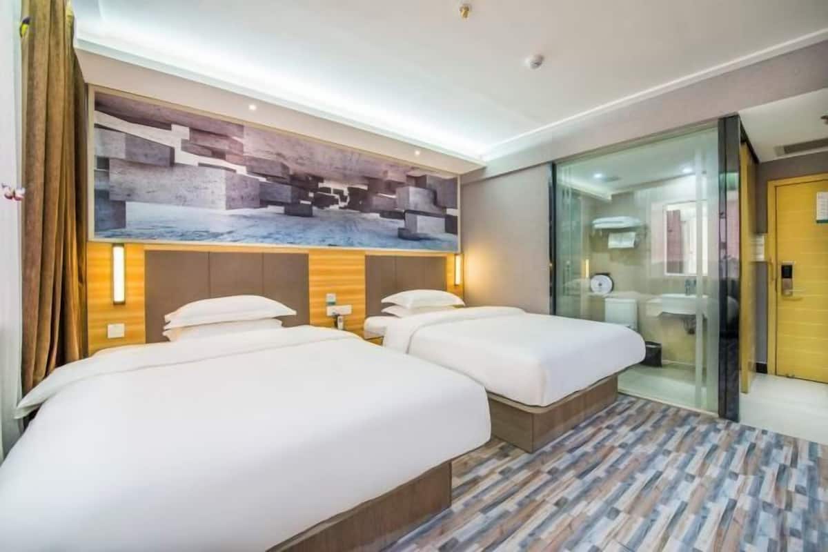 A hotel room with two beds, a modern wall design, and a glass partition separating the room from the bathroom.
