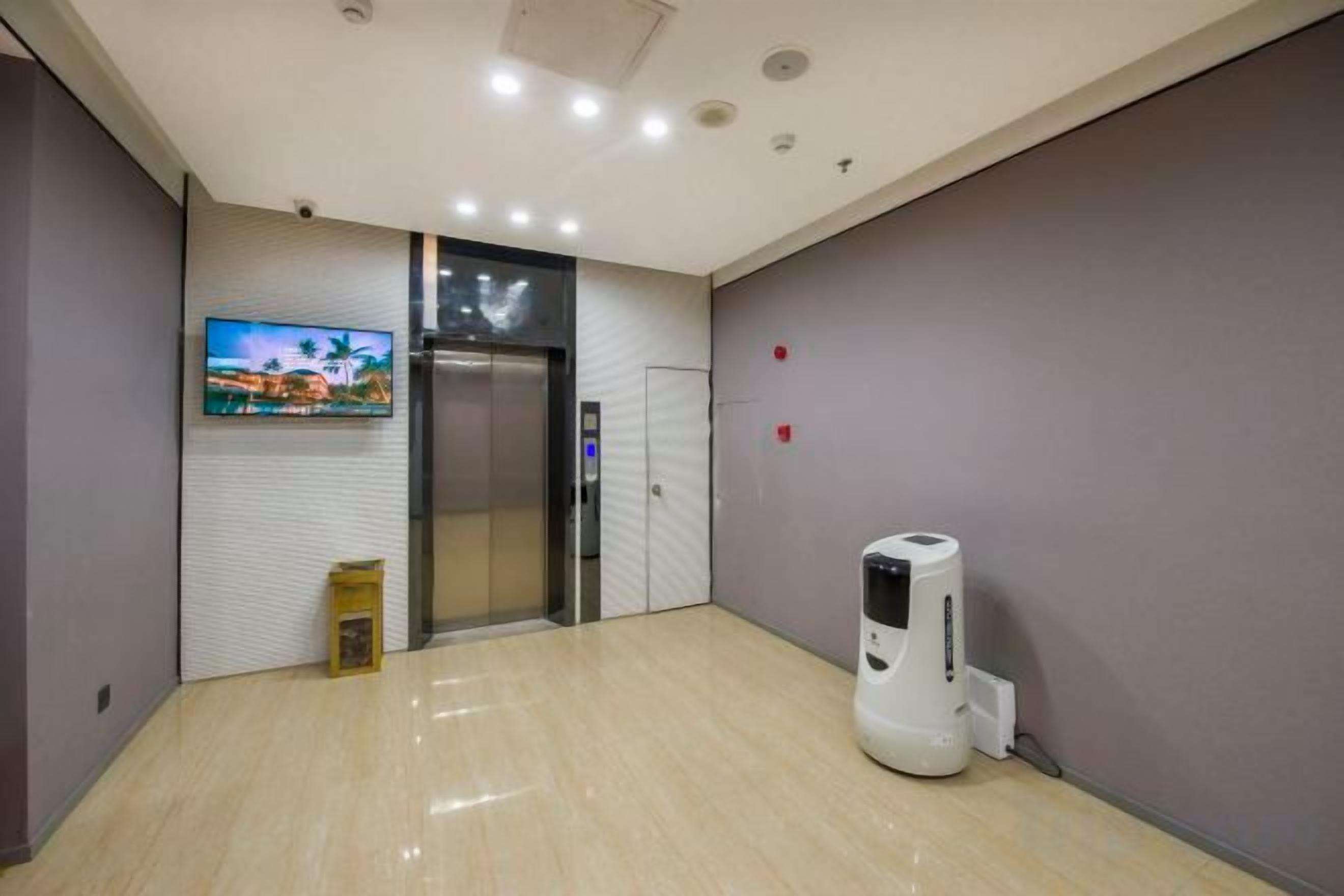 A hotel lobby with a flat-screen TV, an elevator, a trash bin, and a coffee machine.