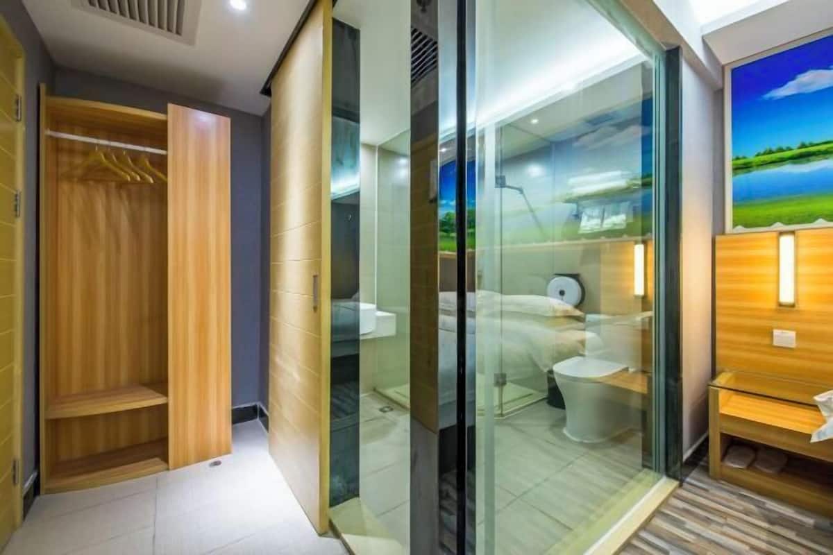 A modern bathroom with a glass shower enclosure, a wooden vanity, and a bed with a white headboard.